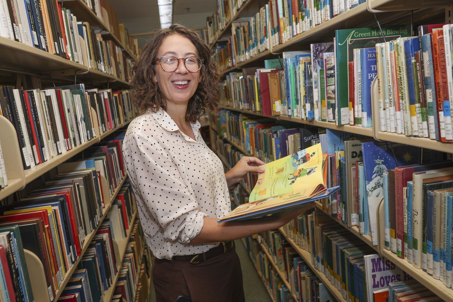 Melanie Walsh holding a picture book in the stacks of a University of Washington library